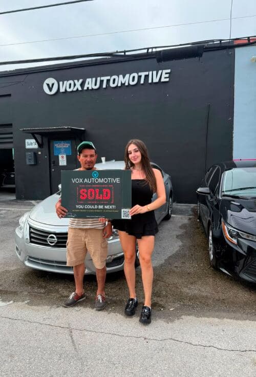 Vox Automotive customer holding a Sold sign next to her new car