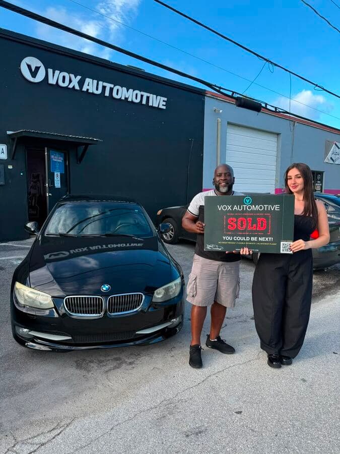 Vox Automotive customers holding a Sold sign in front of a BMW