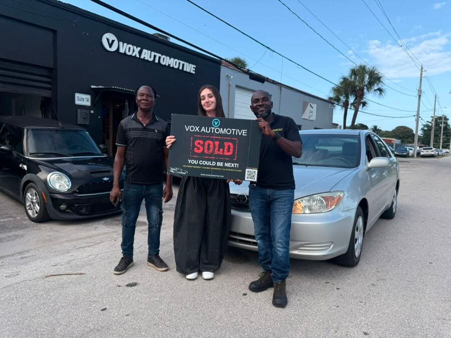 Vox Automotive customers holding a Sold sign in front of a Toyota Camry